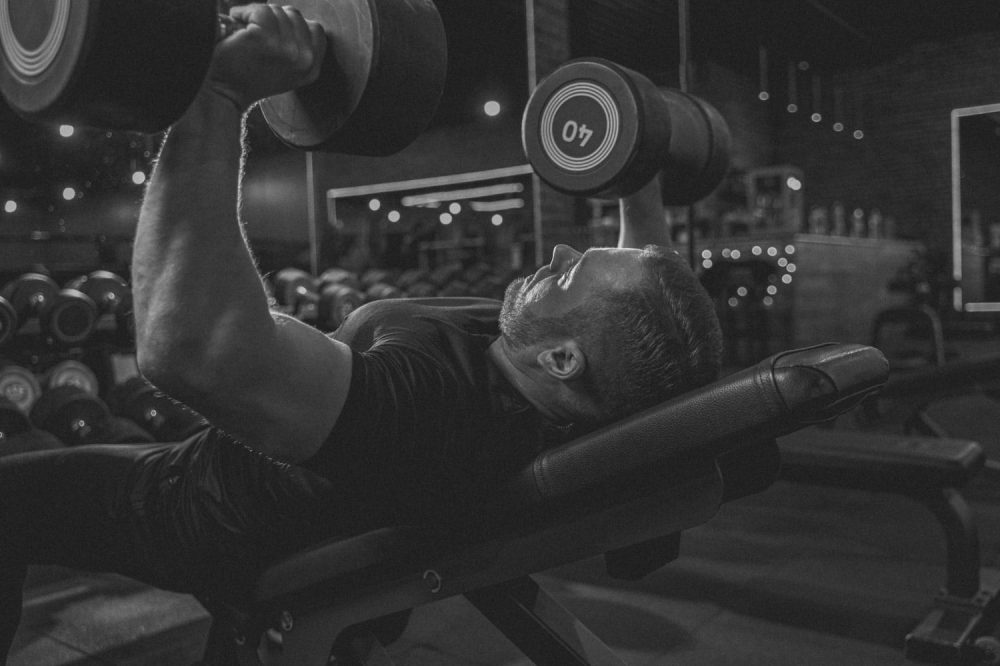 Strong man lying on adjustable weight bench and raising two dumbbells with both arms